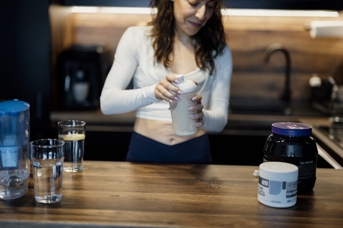 Personne qui prépare un shake protéiné au shaker, pot de whey isolate posé à côté